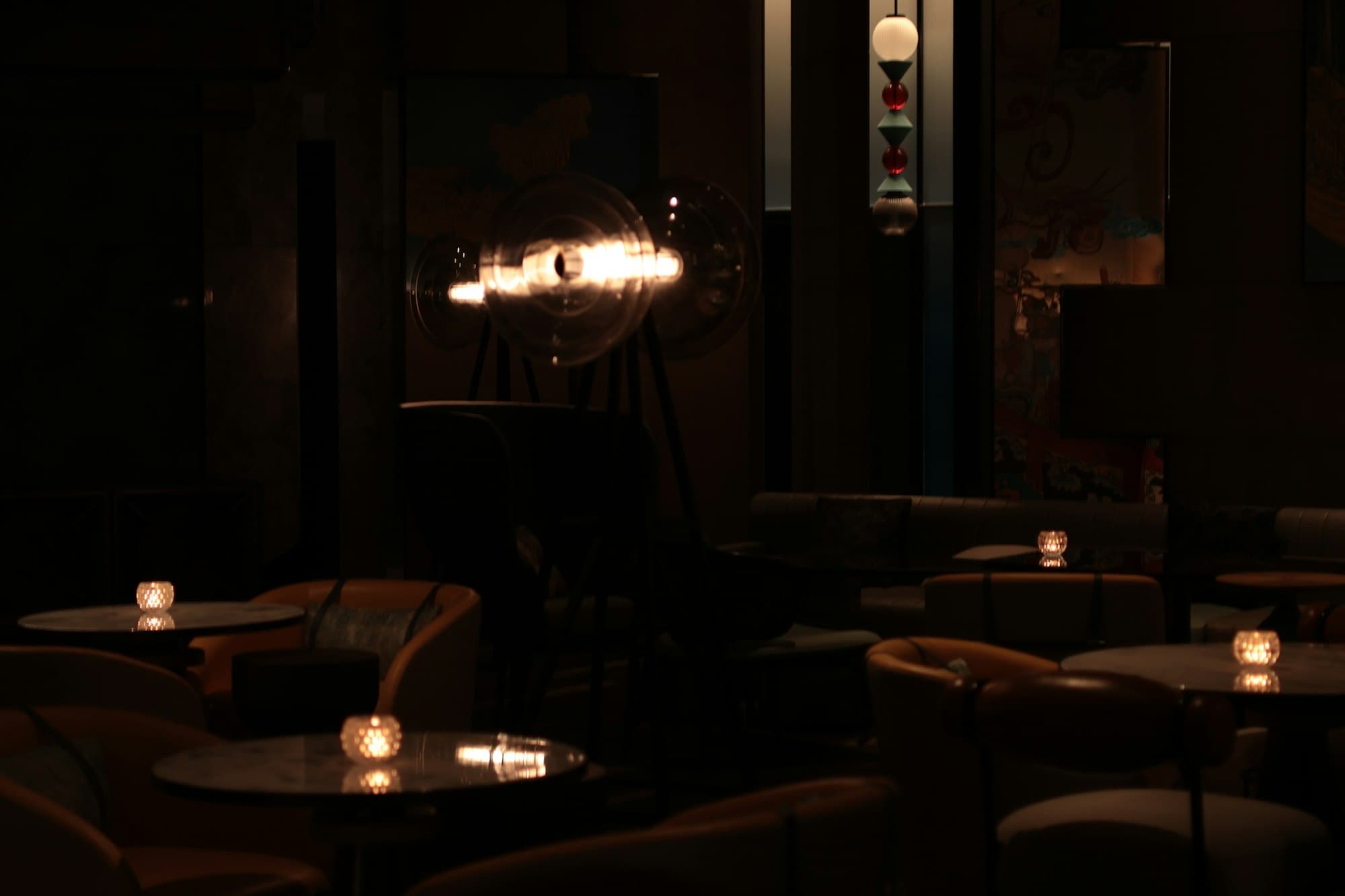 A near-dark dining room lit by small candles on the tables