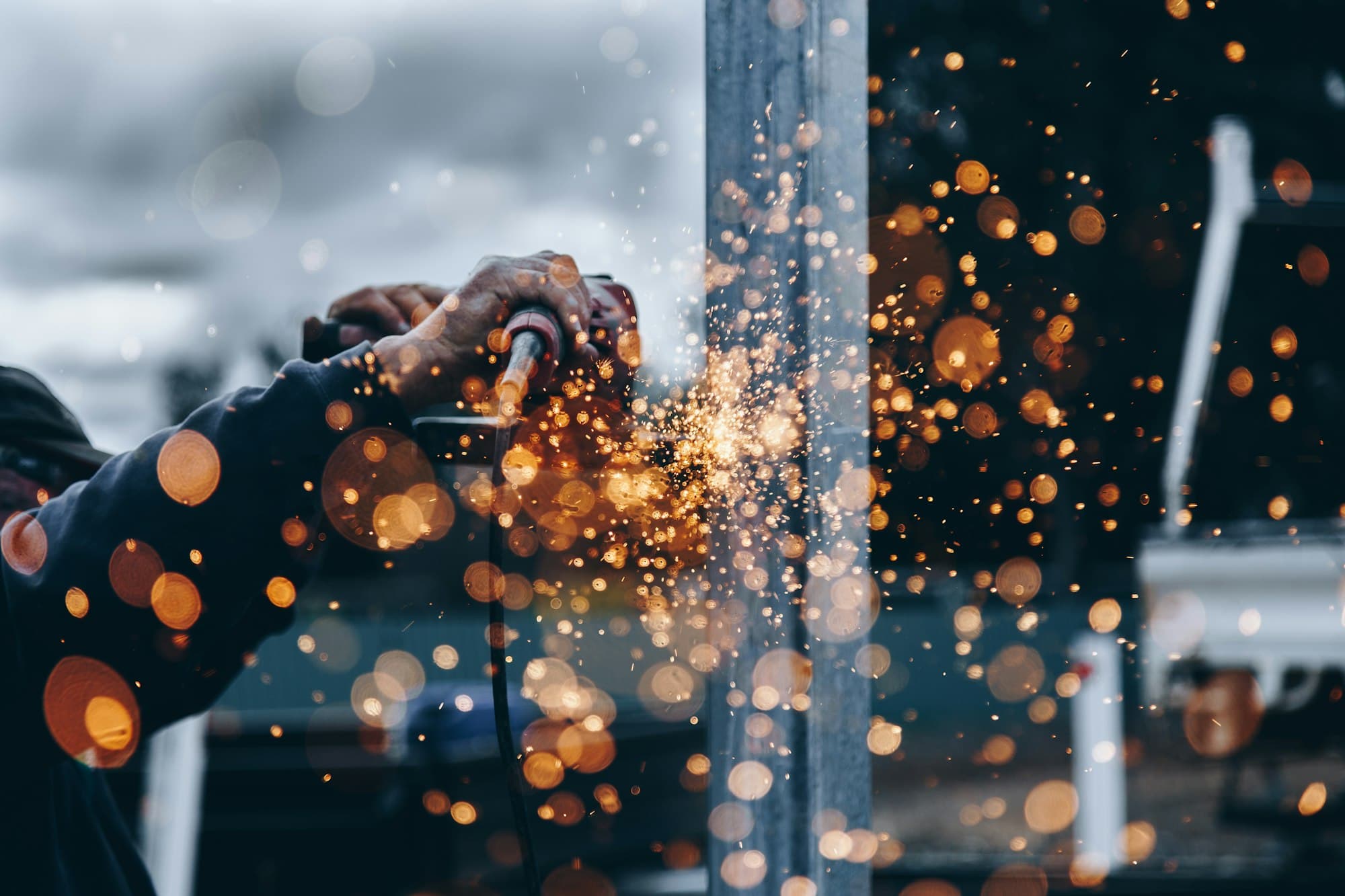A worker's hands guide an angle grinder into a steel post, sparks flying